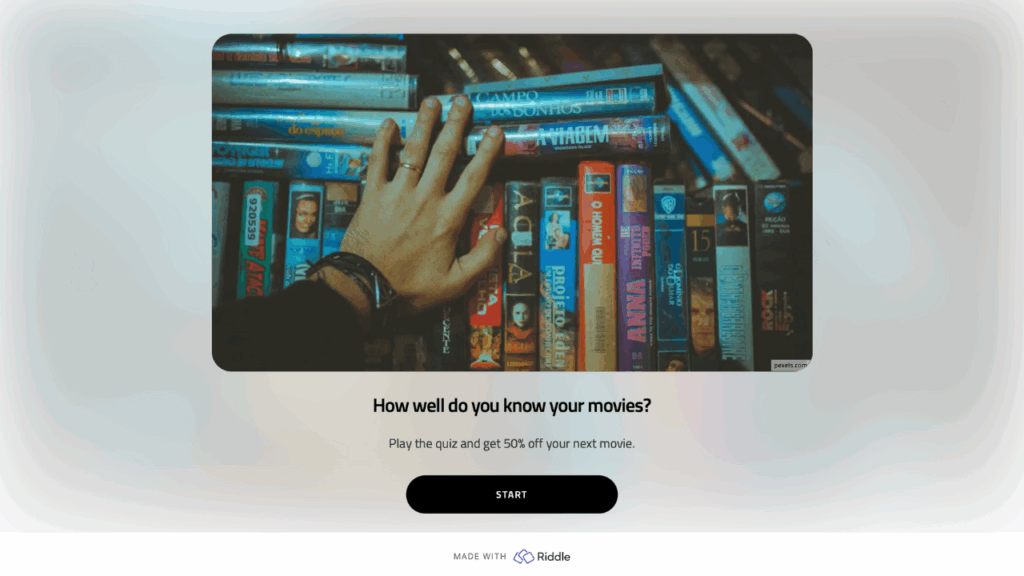 A shelf full of video cassettes, with some piled on top of the row. Someone's left hand is resting on the videos.